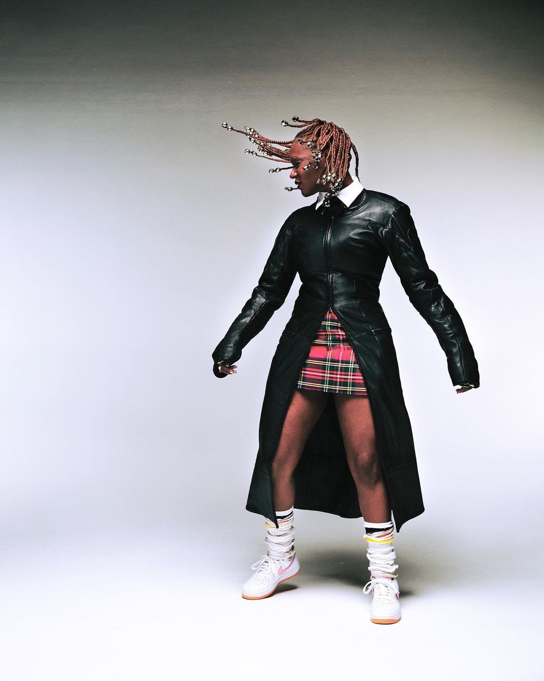 Amaarae in black leather coat with plaid skirt and sneakers